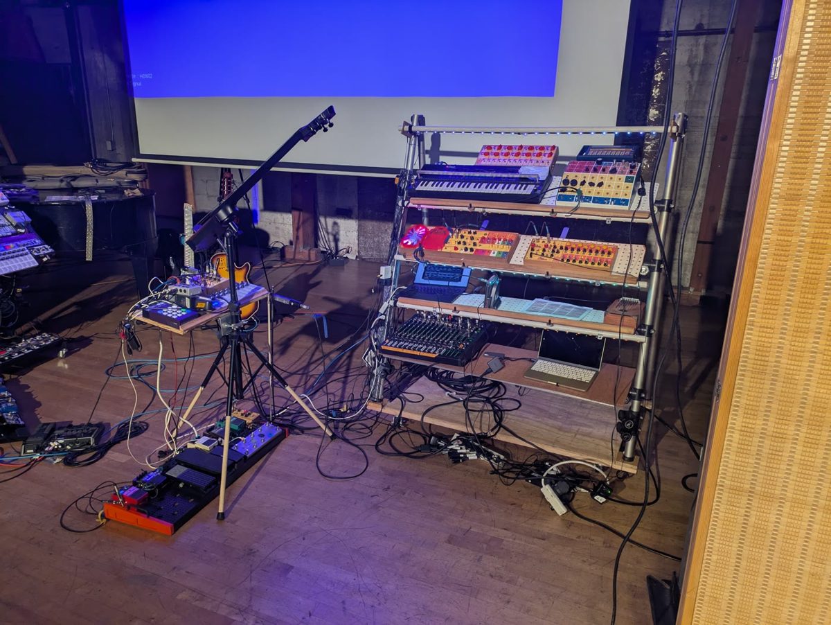 A rack of synthesizers and drum machines on a stage